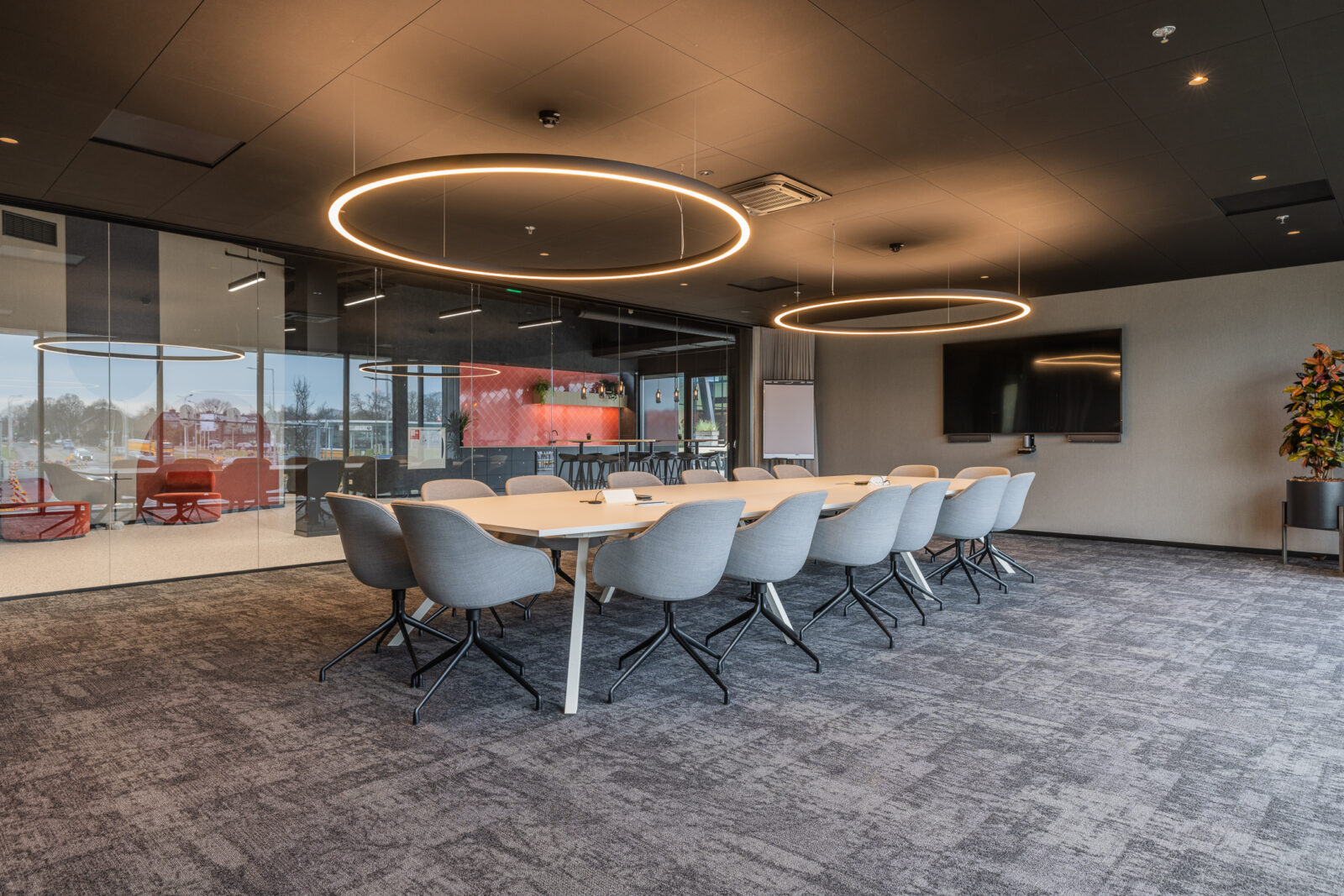 Kadans Science Partner meeting room with circular pendant lights, seating for twelve, and a glazed view into an adjacent lounge.
