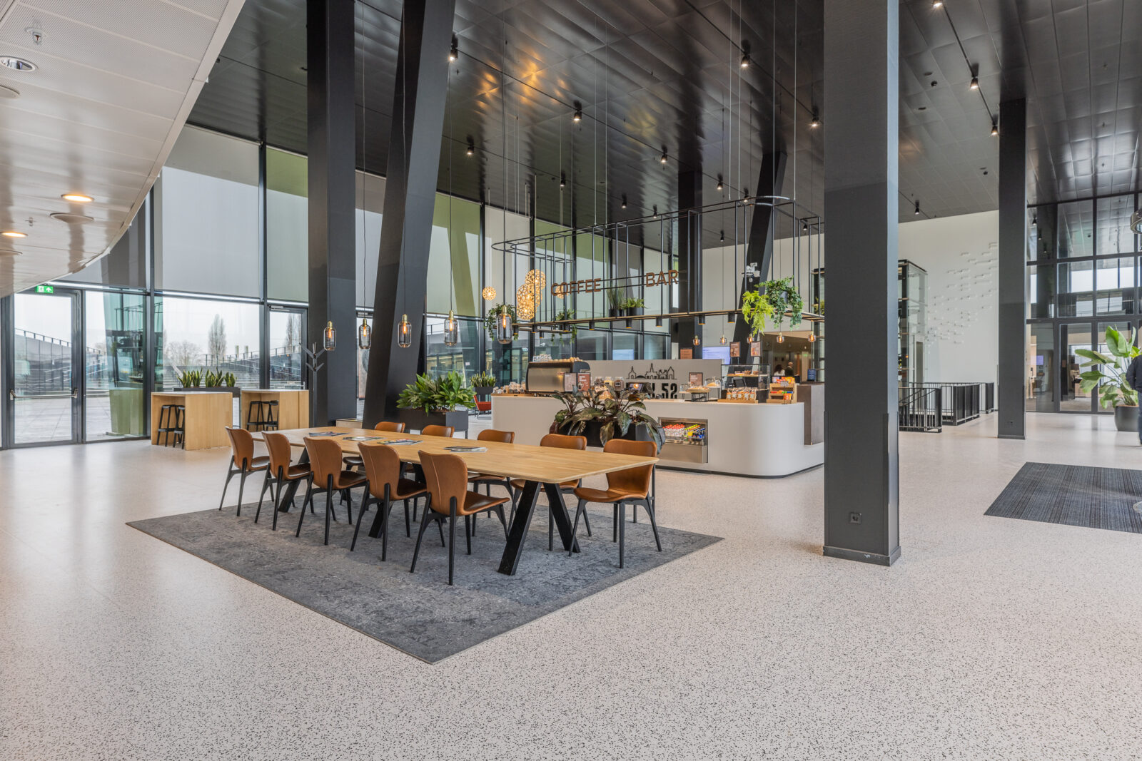 Kadans Science Partner canteen seating area with a communal dining table, coffee bar, pendant lighting, and floor-to-ceiling windows.