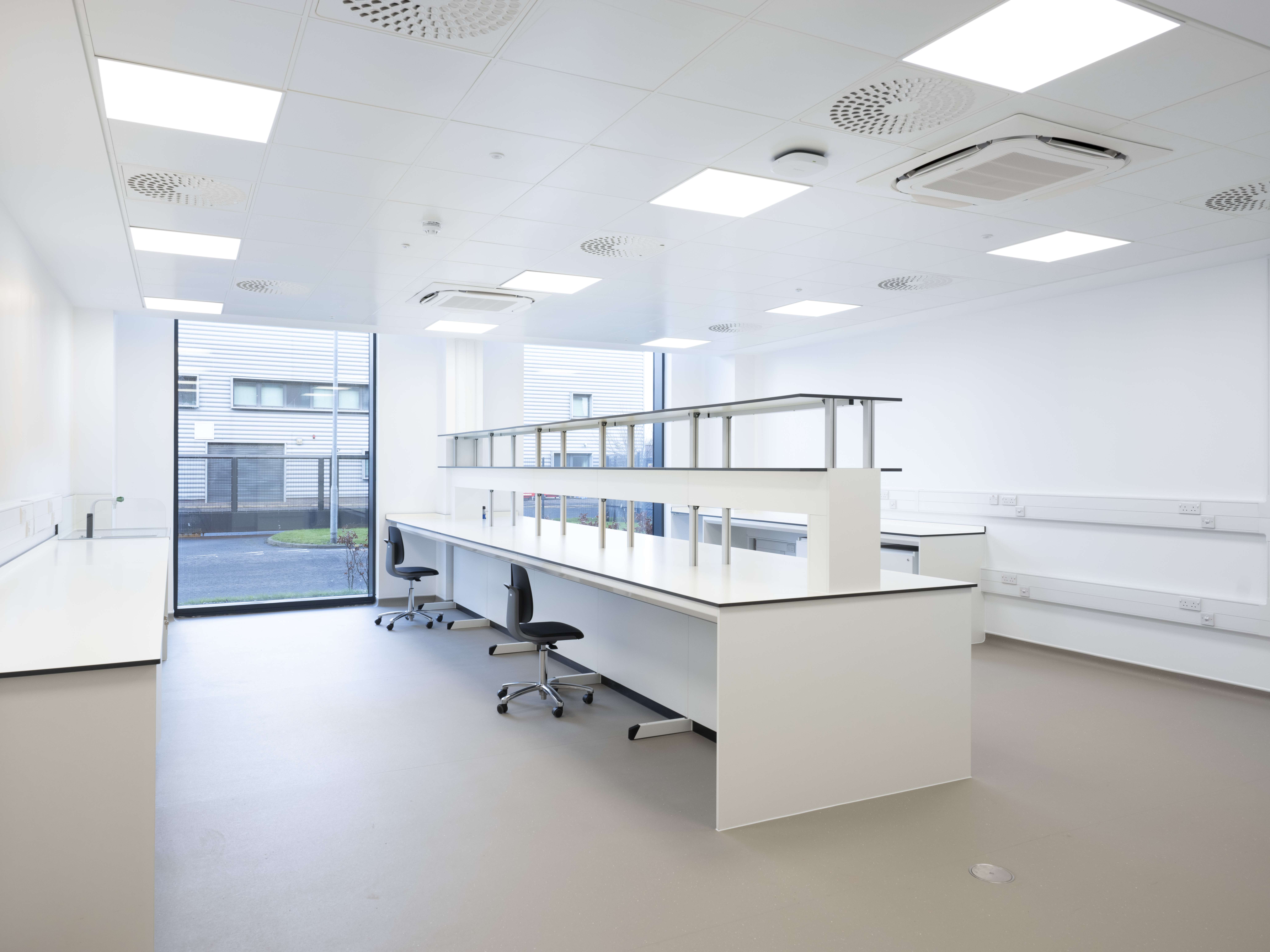 Spacious and bright Kadans Science Partner laboratory with a central island bench, overhead shelving, lab chairs, and garden views.
