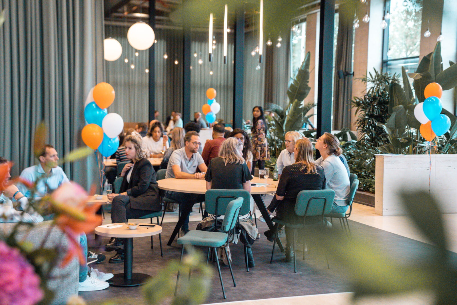 People seated at round tables with balloons at a social event - Kadans Science Partner