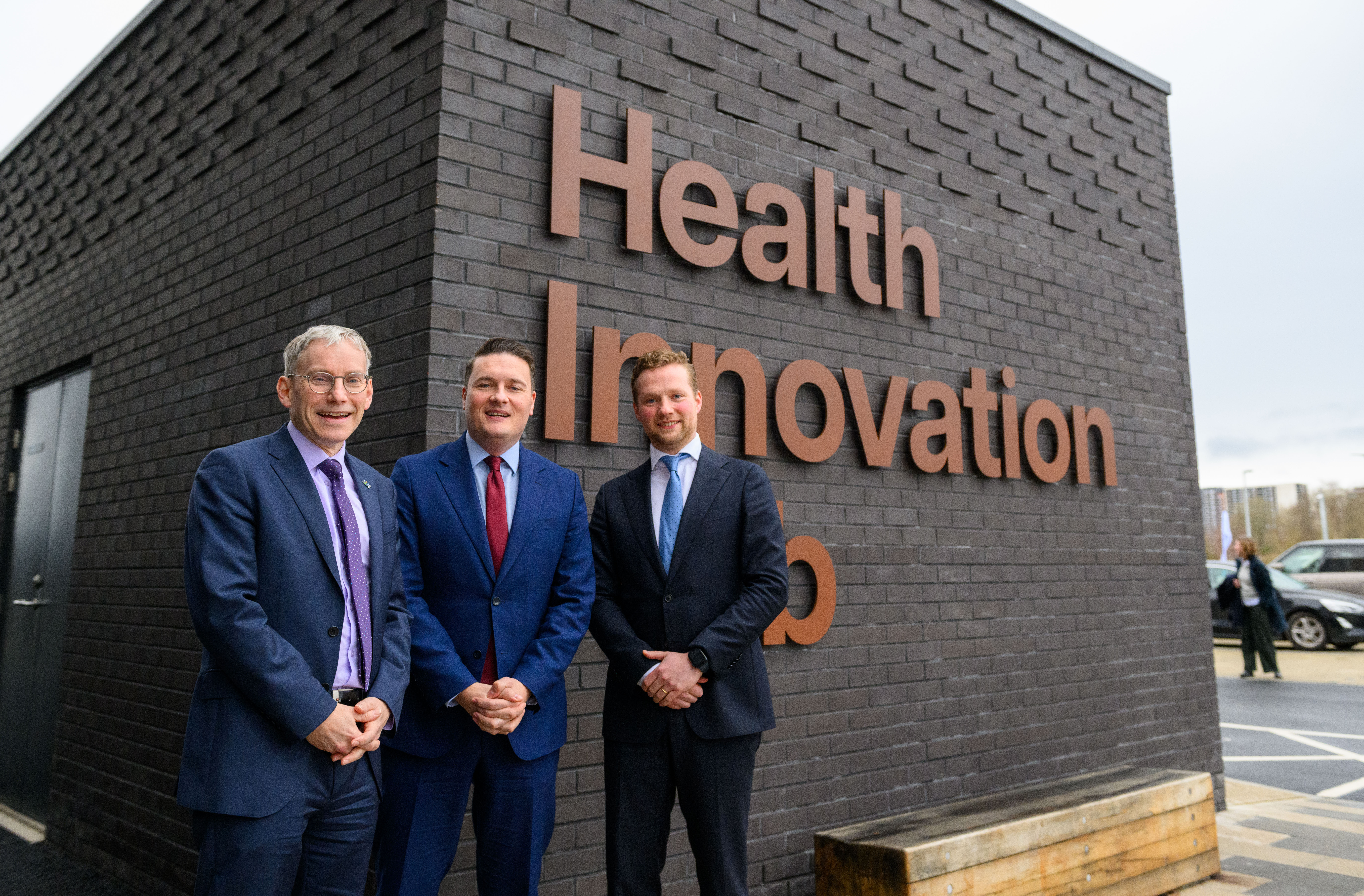 Three men smiling outside the Health Innovation Building
