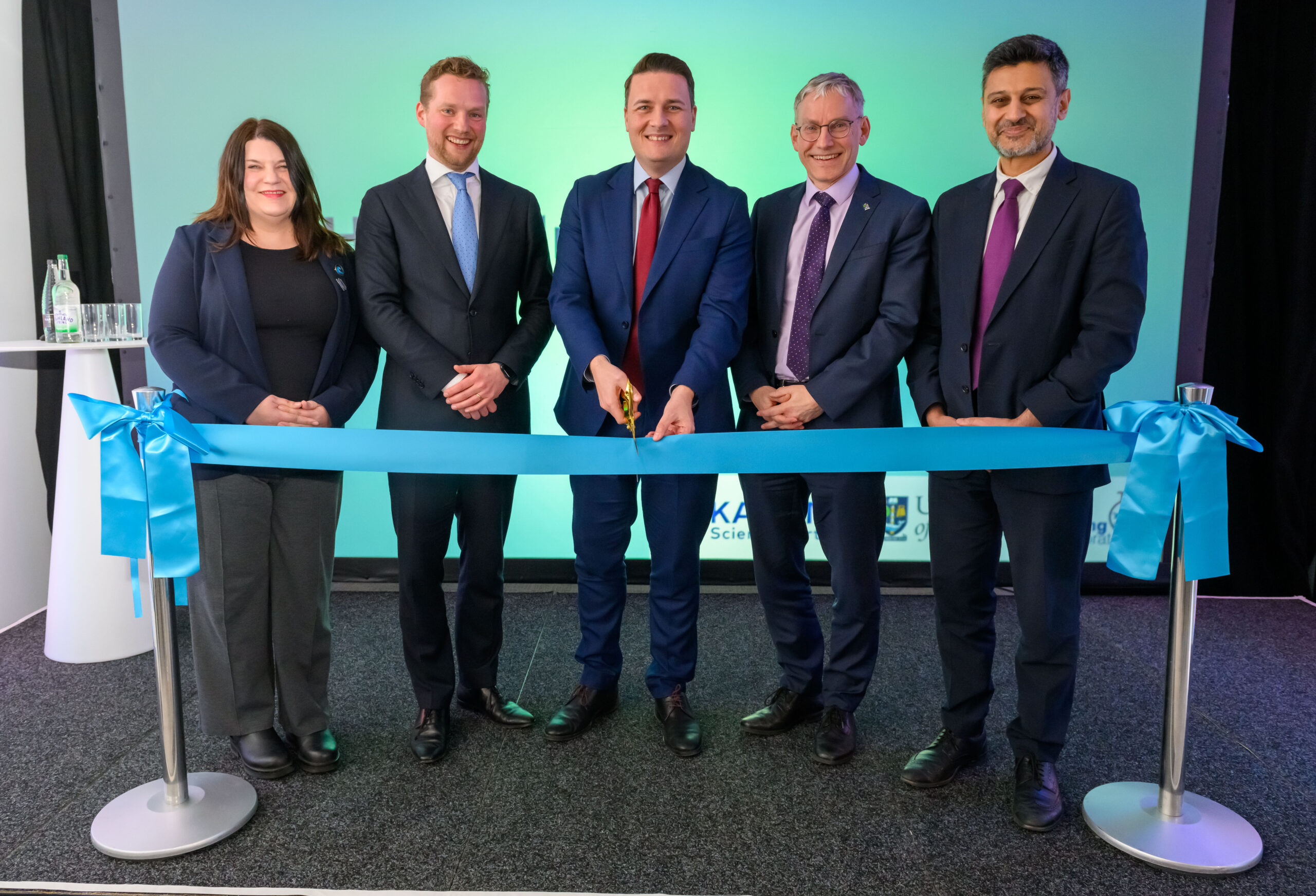 Group of four men and one woman at ribbon cutting as a blue ribbon is cut