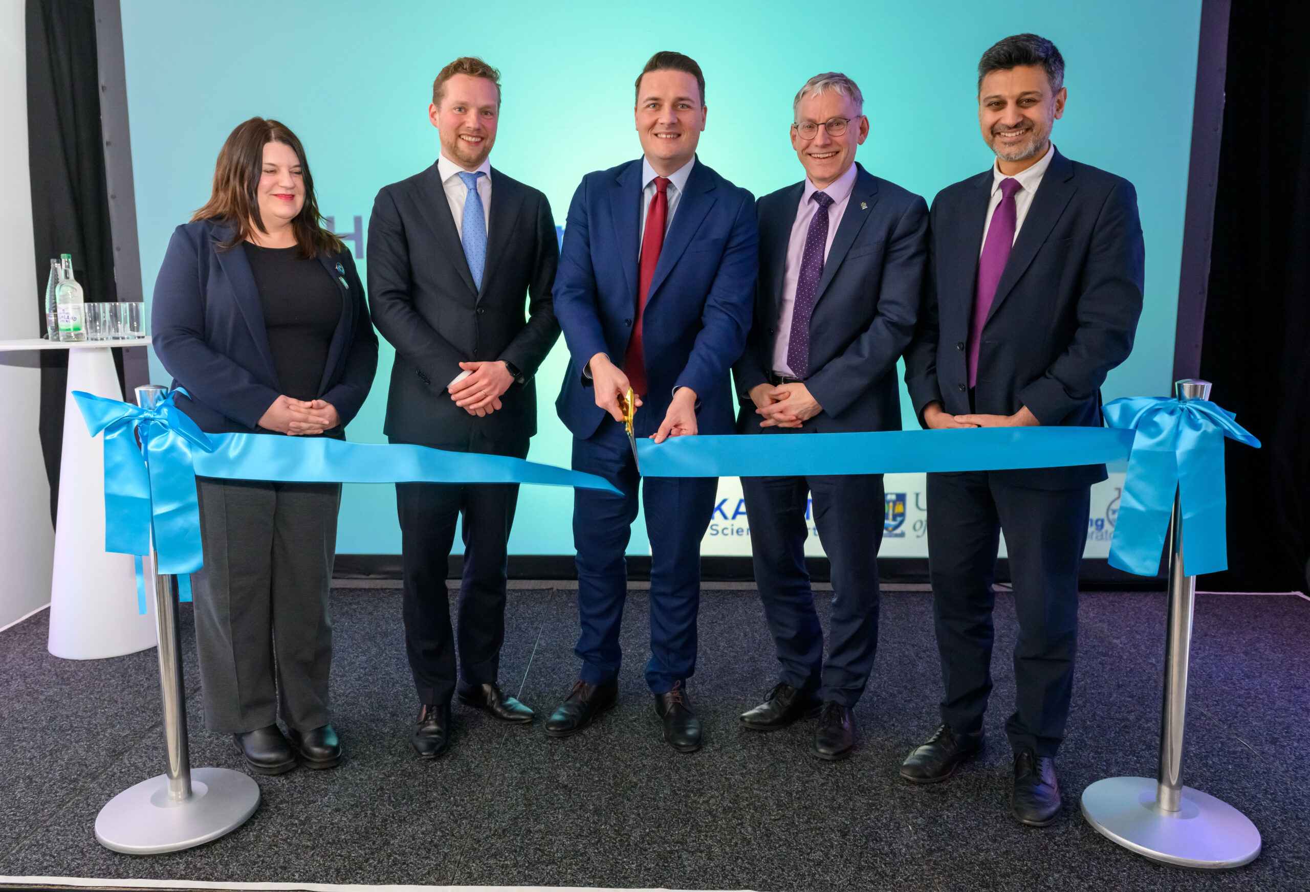 Ribbon cutting ceremony with four men and one woman as one man cuts a blue ribbon