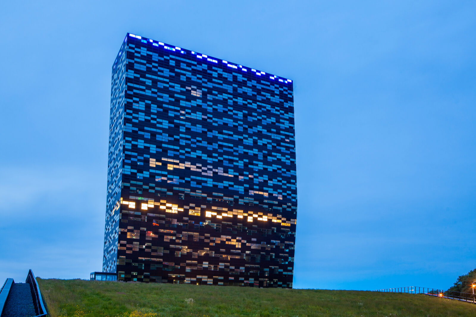 The Kadans Science Partner tower in Nijmegen illuminated at dusk, with blue rooftop lighting and warm glowing windows.