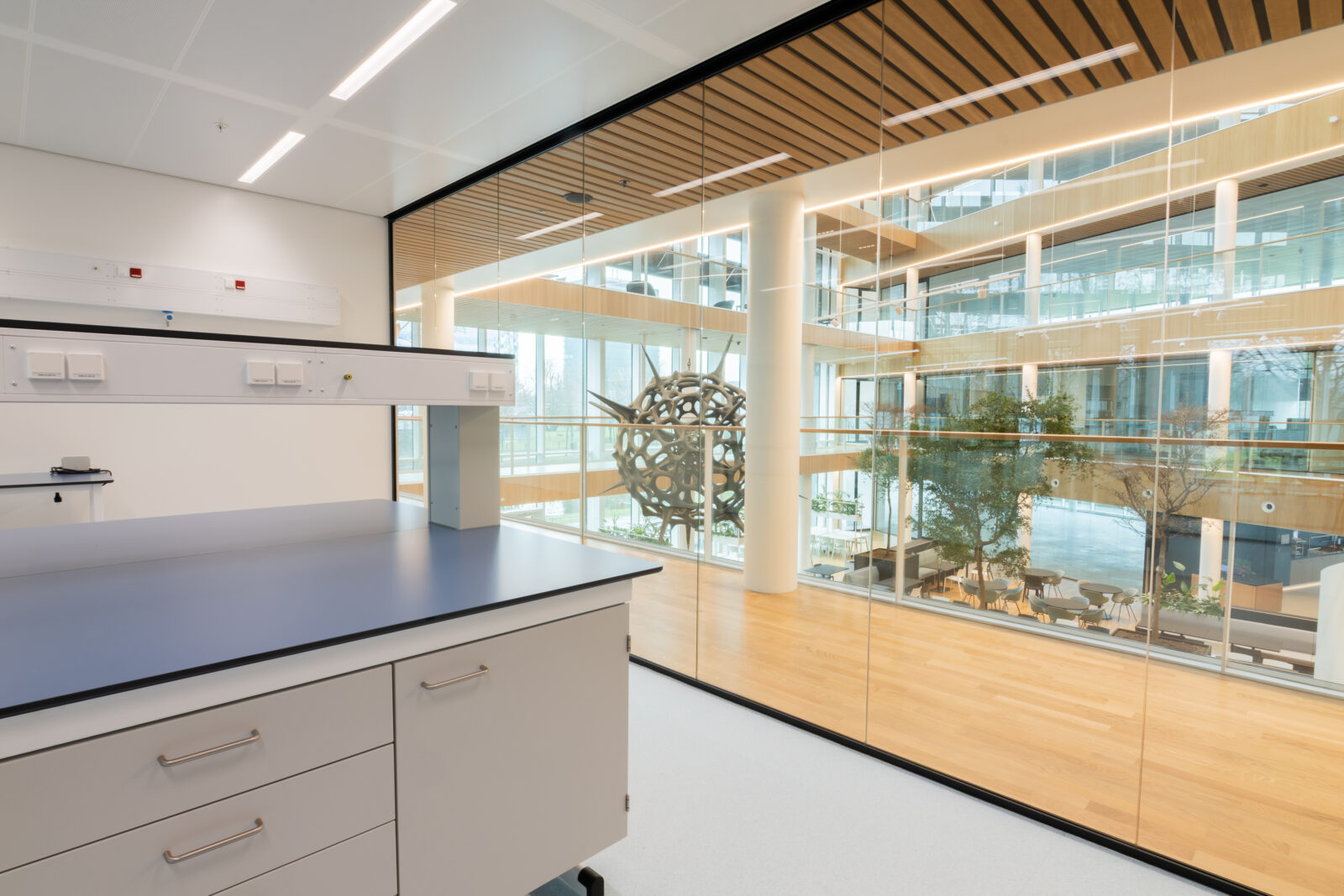 Lab space at Plus Ultra Utrecht with workbench and view through glass wall into atrium